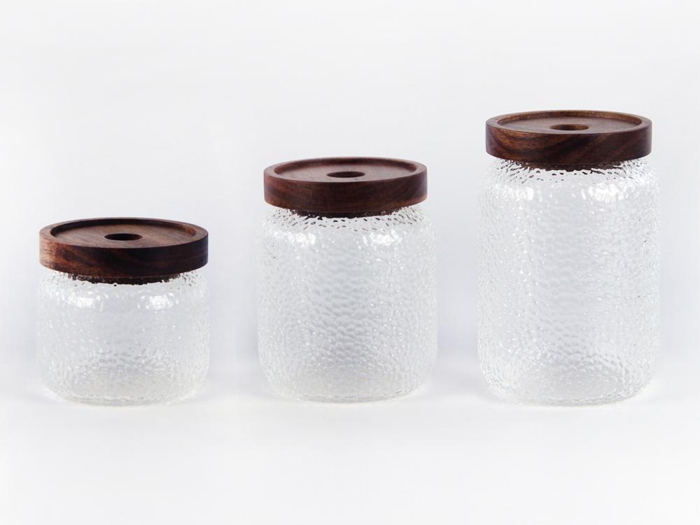 Three clear textured glass jars of different heights with wooden-looking lids